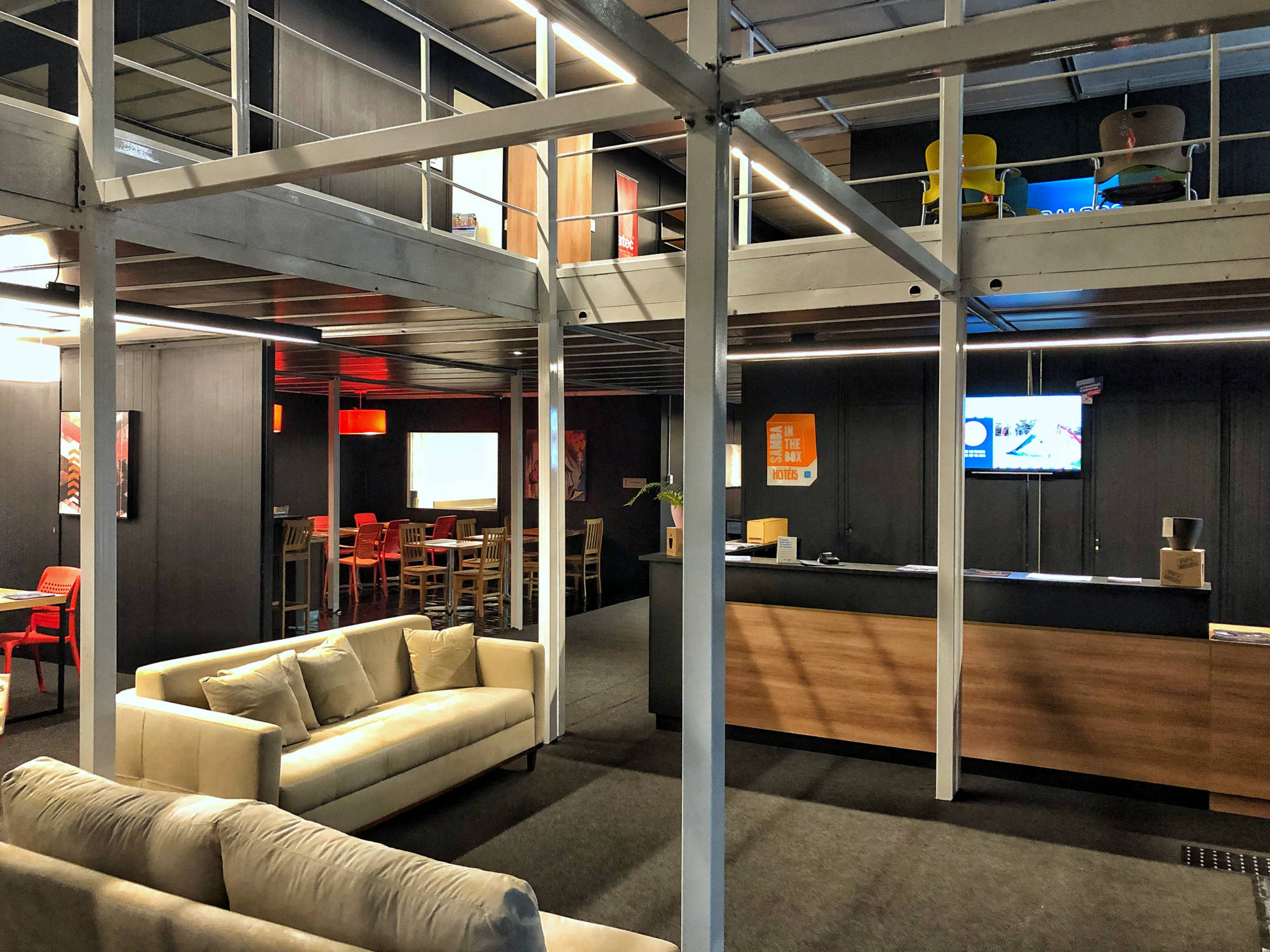 Recepção de hotel em container criado pela POKT Design+Arquitetura, montado em apenas 6 dias na feira Sirha em São Paulo, com conceito modular, sustentável e adaptável para temporadas e festivais de música.